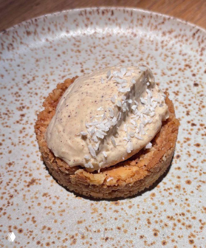 Небольшой десерт: корж с кремом и кокосовой стружкой на тарелке — фотография финального блюда ужина в Tacobar