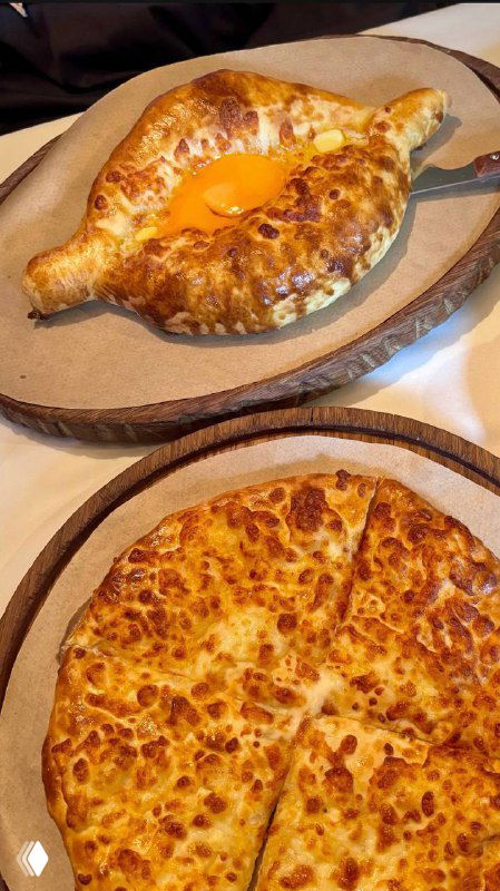 Хачапури на круглом блюде с румяной корочкой и жидким желтком в центре, вид сверху, деревянная подложка и тёплая подача.