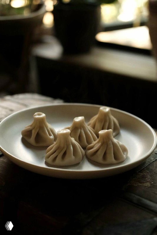 Тарелка с пятью аккуратно слепленными хинкали на тёмном фоне, видно складки теста и пышную форму, вид сбоку.