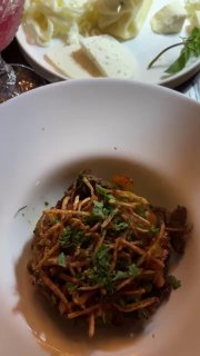 Небольшая порция тёплого блюда с тонко нашинкованными ингредиентами и зеленью — одна из домашних закусок ресторана.