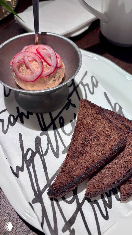 Закуска в маленькой кастрюльке с маринованным луком и ломтиком тёмного хлеба на тарелке — текстура и сервировка бистро.