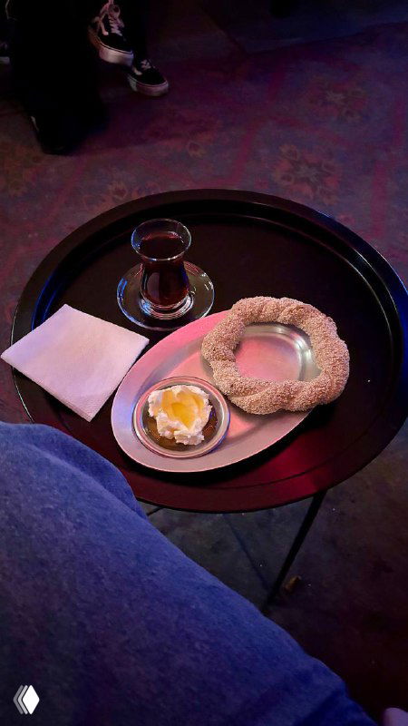 Крупный план подачи: симит с кунжутом, мисочка каймака с медом и стакан чая на круглом подносе, уютный тёплый кадр.