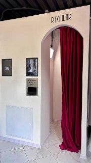 Интерьер фотостудии: вход в классическую фотобудку с красной занавеской, аппарат для печати на стене и оформление зоны съёмки.