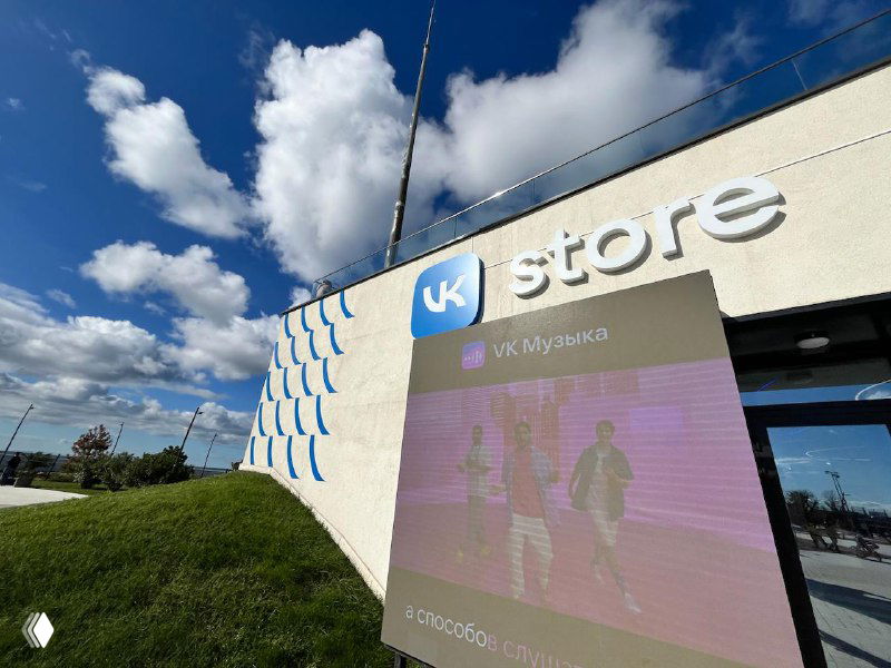 Внешний вид VK store рядом с коворкингом: вывеска "VK store", рекламный экран у входа и архитектурные элементы фасада на фоне чистого неба.