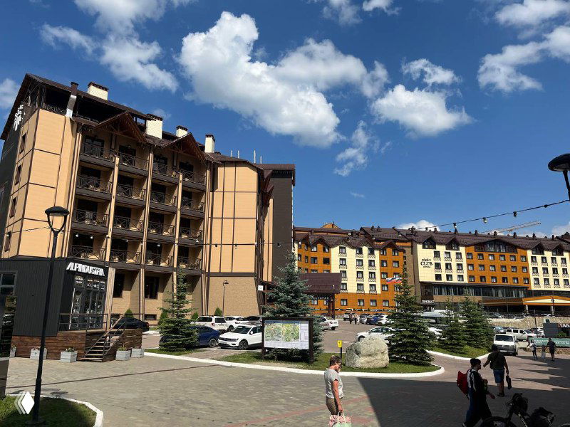 Пешеходная зона курортного квартала Архыза с отелями и магазинами: благоустроенная площадь, гости и вывески гостиниц на солнечном дне.
