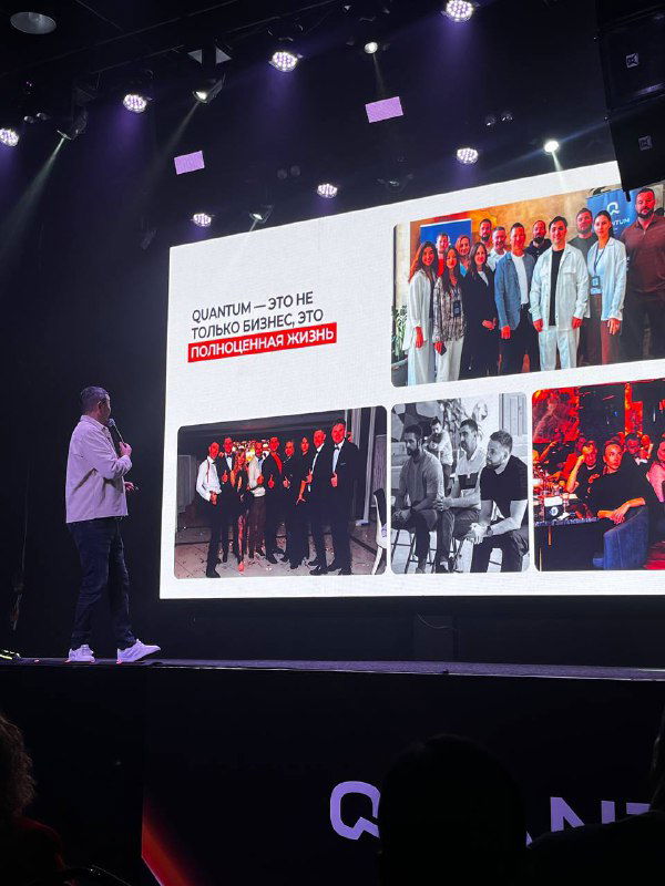 Широкий кадр сцены и большого экрана с коллажем слайдов: докладчик стоит слева, видна презентация и затемнённый зал с слушателями.