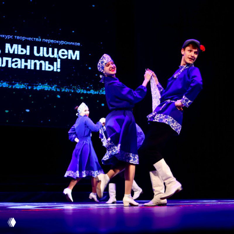 Танцевальный коллектив в ярких народных костюмах исполняет номер на сцене конкурса первокурсников, динамичный кадр с артистами в движении и улыбках.