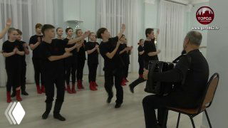 Юные артисты ансамбля «Русские узоры» поют и двигаются в зале под аккомпанемент баяниста — коллектив на конкурсе или репетиции.