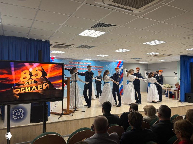 Дети и подростки выступают на сцене Кванториума «Дружба» во время юбилейного концерта Центра туризма; на экране видно «85 лет. Юбилей».