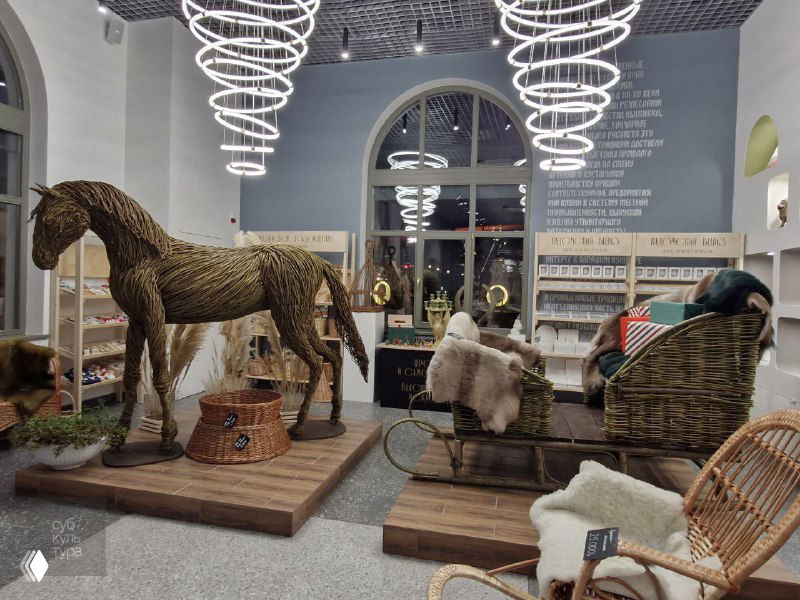 Интерьер «Резиденции традиций» в Рязани: большая плетёная лошадь и сани на выставочной платформе, рядом полки с праздничными сувенирами и декором.