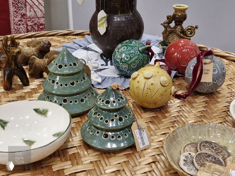 Керамические ёлочки, шарики и декоративные предметы на плетёной корзине в витрине: сувениры и новогодние декоры от рязанских мастеров вблизи.
