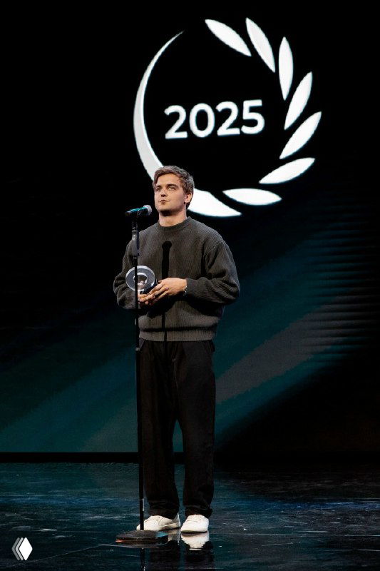 Максим Исаев держит награду у микрофона на сцене премии «Блогема» 2025, момент речи победителя и вручения приза.