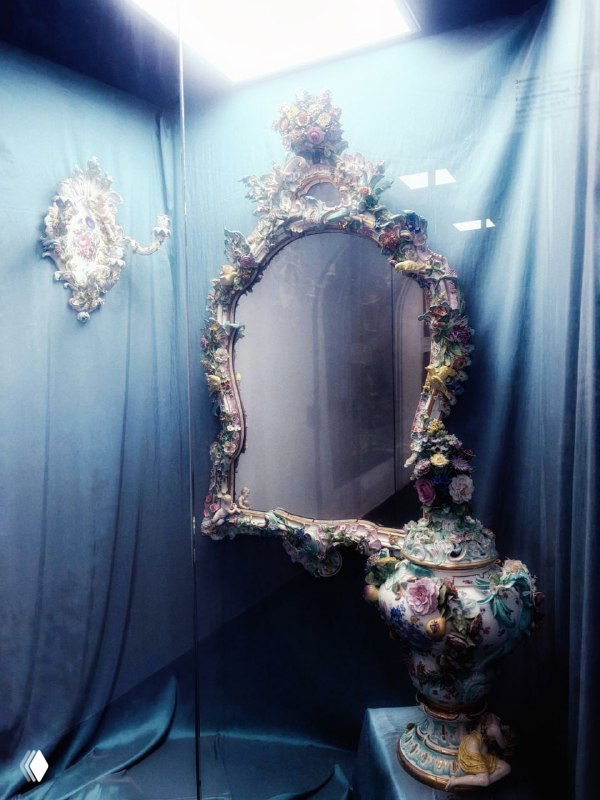 Фотография антикварного зеркала желаний в витрине Рязанского художественного музея с резной цветочной рамой и декоративным постаментом.