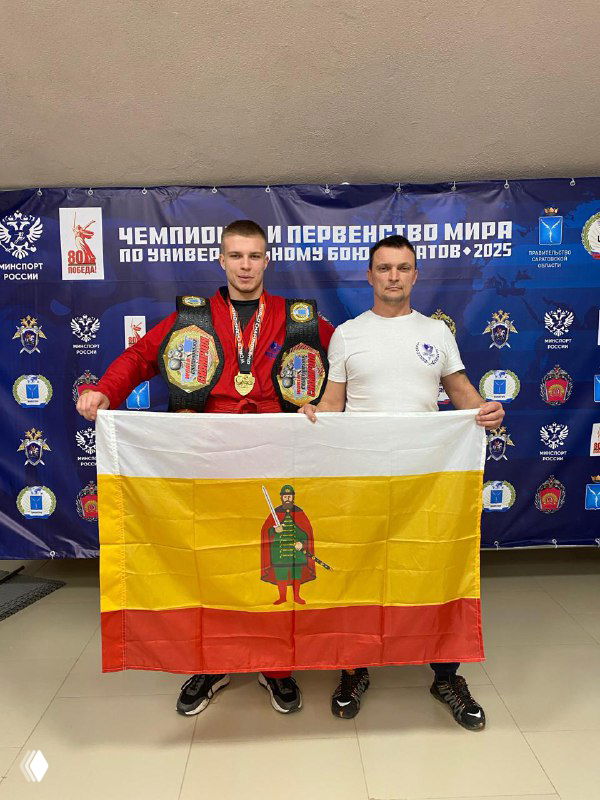 Два спортсмена держат жёлто-красный флаг Рязанской области на фоне баннера чемпионата; видны медали и спортивная форма участников.