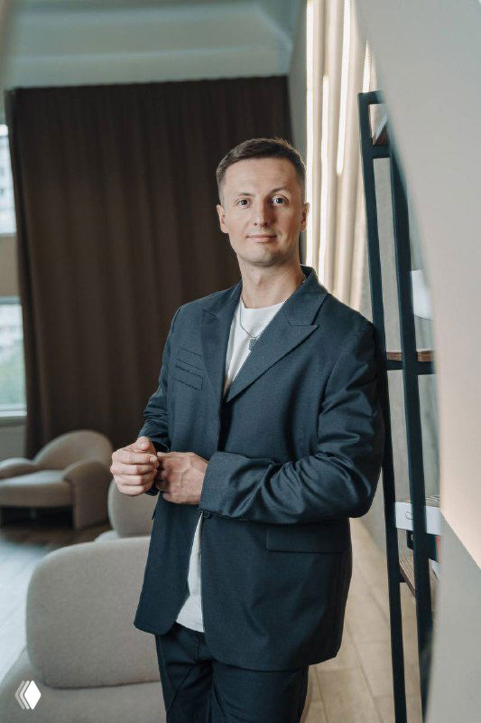 Портрет автора в деловом костюме в офисной обстановке: мужчина стоит у перил, спокойный фон, профессиональный образ