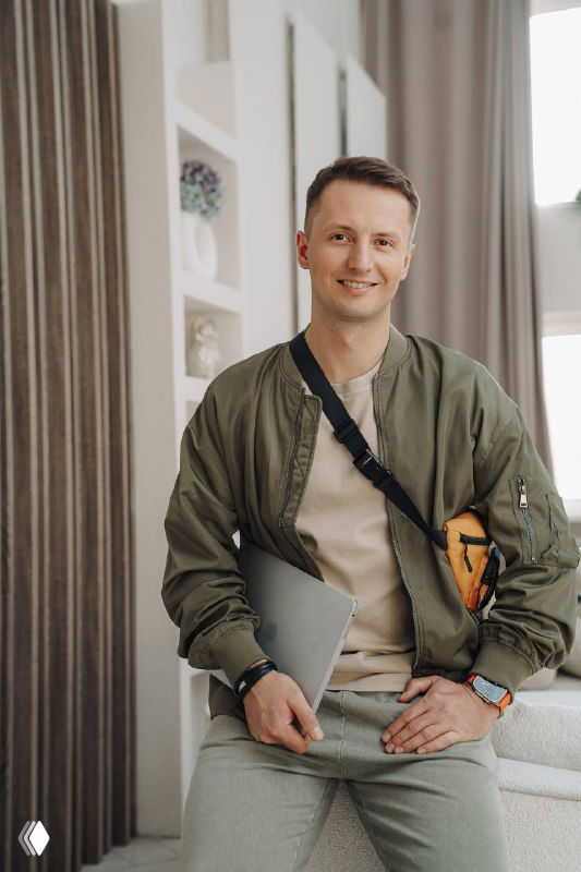 Мужчина в повседневной одежде с ноутбуком и сумкой через плечо, сидит в светлом офисном интерьере; иллюстрация деловой тематики.