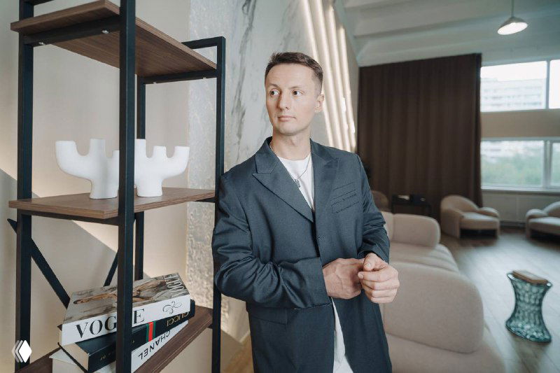 Деловой портрет: мужчина в пиджаке в светлом офисном интерьере рядом со стеллажом с журналами, иллюстрация бизнес‑контекста.