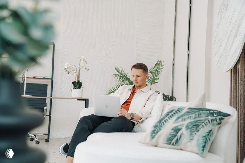 Мужчина в светлом офисном пространстве сидит на диване с ноутбуком — иллюстрация автора, символизирующая работу с продажами.