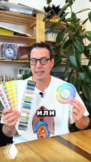 Дизайнер в мастерской держит поставщицкий цветовой веер и круг Иоханнеса Иттена на фоне стеллажей с образцами и зелёного растения.