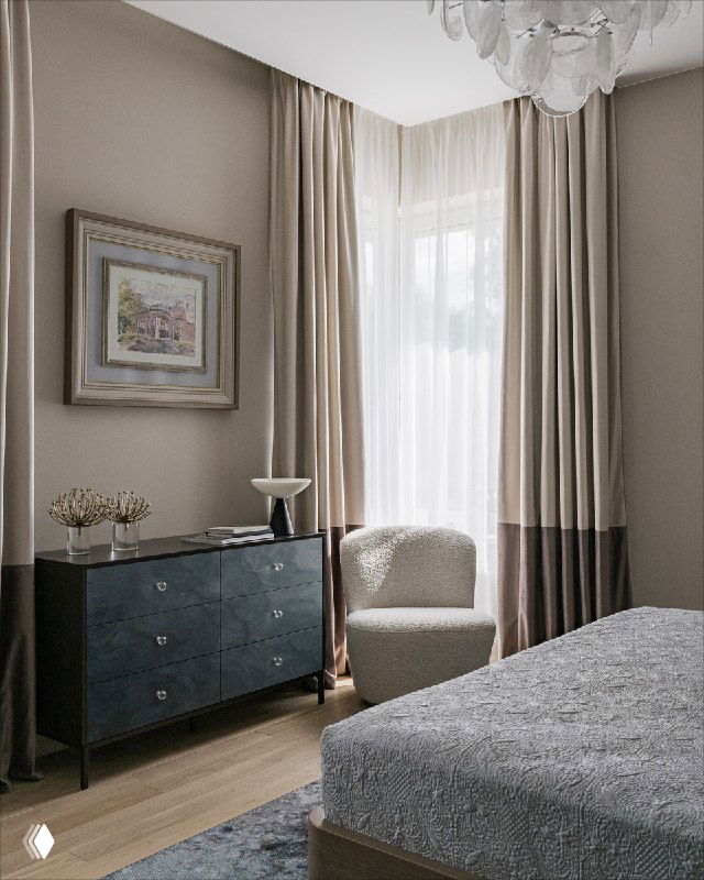 Комод с расписными фасадами и картина в багете над ним, светлые шторы, кресло у окна и естественное освещение, подчёркивающее фактуру материалов в спальне.