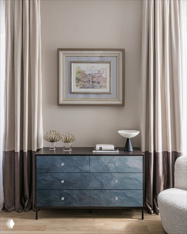 Классический комод с синей тонировкой фасадов, декоративные аксессуары на столешнице и картина в рамке на фоне портьер — элегантная композиция комнаты.