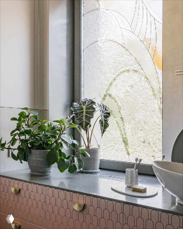 Фрагмент окна с витражной росписью крупным планом: эффект изморози и растительных форм, свет создаёт мягкие тени на подоконнике и растениях.