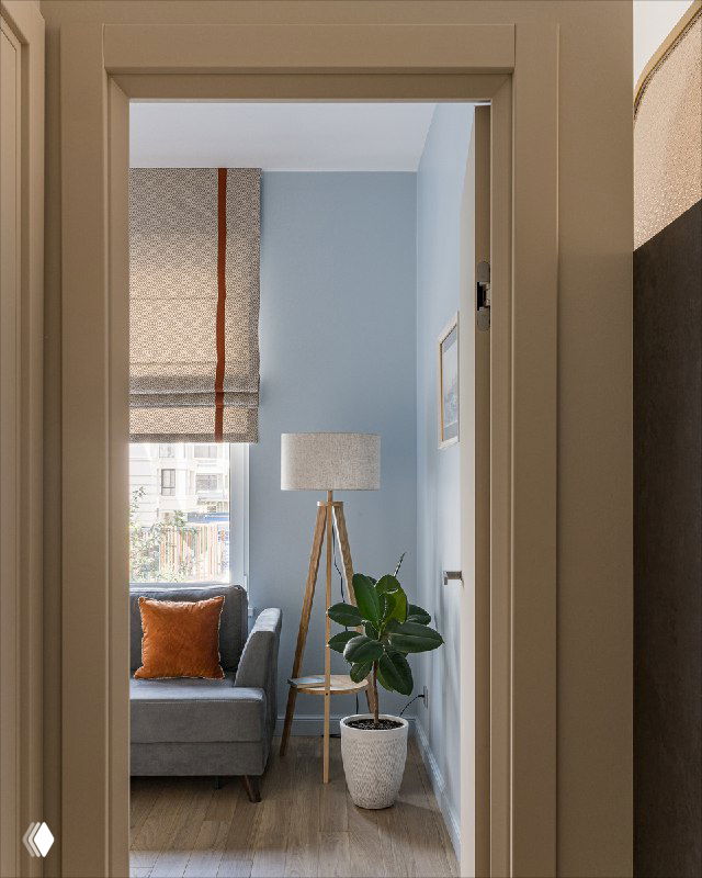 Вид через дверной проем на гостевую комнату: римская штора на окне, диван с оранжевой подушкой, напольный торшер и фикус у нежно-голубой стены.