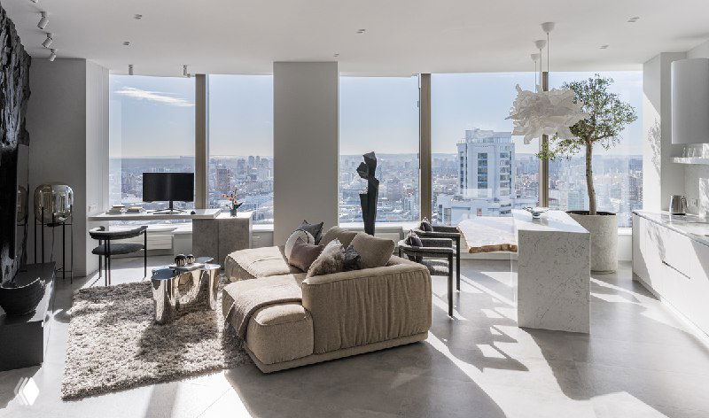 Светлый современный интерьер гостиной проекта «Швейцарские Альпы» с панорамными окнами, мягкой мебелью и видом на городской пейзаж