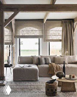 Гостиная в нейтральных тонах с римскими шторами и диваном; натуральные ткани, мягкий свет и бежевые оттенки создают уютную атмосферу.