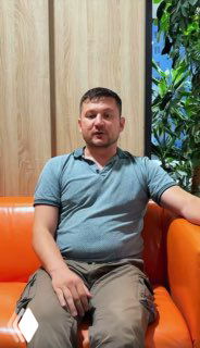 Портрет прораба Семена: мужчина на оранжевом диване на фоне деревянной панели и зелёных растений в интерьерной обстановке.