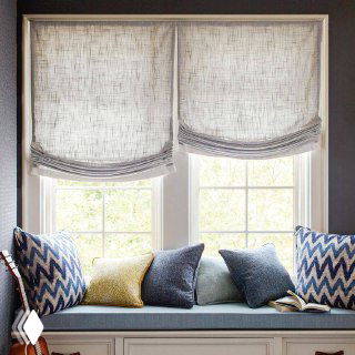 Подоконная зона с мягким сиденьем и подушками, над ней полупрозрачные светлые римские шторы, создающие уютное место для чтения.