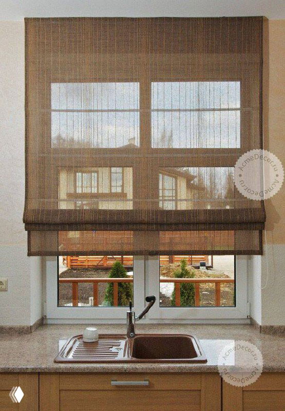 Кухонное окно с коричневыми тканевыми римскими шторами; опущенные шторы демонстрируют фактуру и тёплые оттенки древесины на фоне.