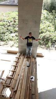 Иван Безруков стоит на длинных строительных досках внутри недостроенной части дома; видны деревянные балки, лестница и зелёная растительность за пределами стен.