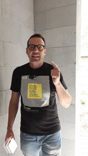 Иван Безруков в очках и чёрной футболке на фоне стены указывает пальцем и держит смартфон — о значении постирочной в доме.