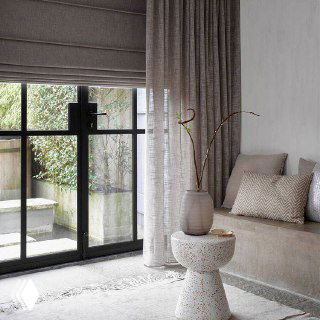 Современная гостиная с большими окнами и бежевыми римскими шторами в сочетании с длинными шторками; натуральные текстуры и мягкие ткани.