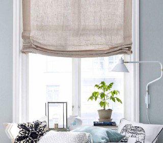 Светлое окно с льняной римской шторой, подушка на подоконнике и настенная лампа — интерьер в пастельных, спокойных тонах.