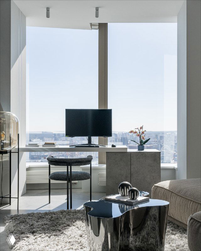 Рабочее место у панорамного окна с видом на город: стол у окна, монитор, минималистичная зона для работы и многое панорамное остекление.