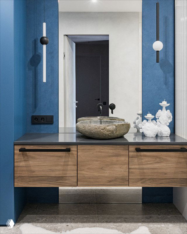 Интерьер мастер-ванной: круглая каменная раковина на столешнице, деревянные выдвижные фасады и синяя фактурная стена с зеркалом над тумбой.
