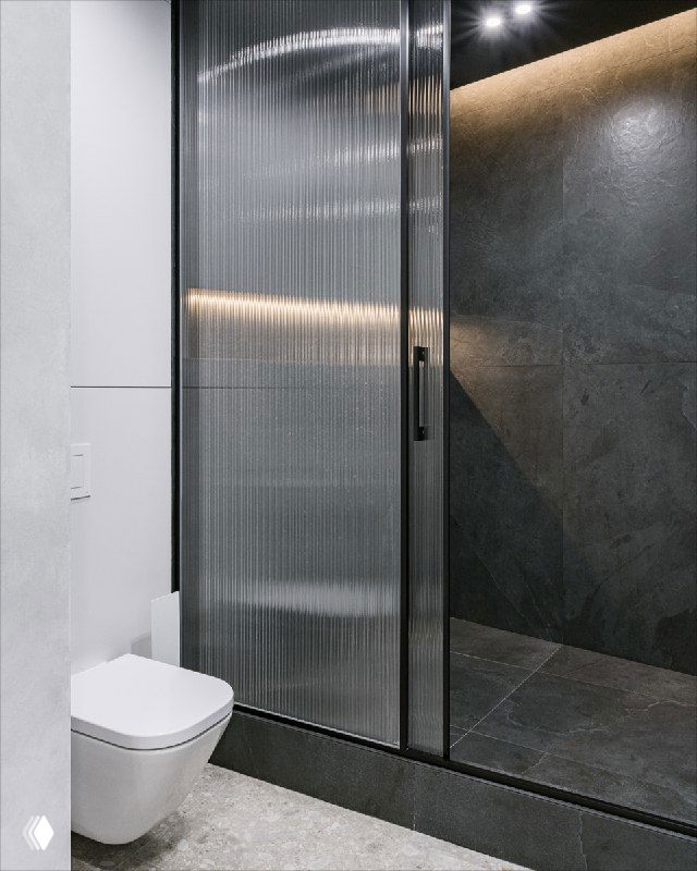 Душевая комната с рифлёным стеклом и тёмной фактурной облицовкой стены; вид на душевую кабину и расположенный рядом санузел.