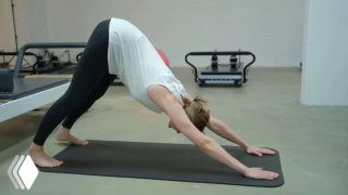 Кадр из видеообзора: интерьер пилатес‑студии «Культура тела», женщина выполняет асану «собака мордой вниз» на коврике, видны реформеры и минималистичный пол.