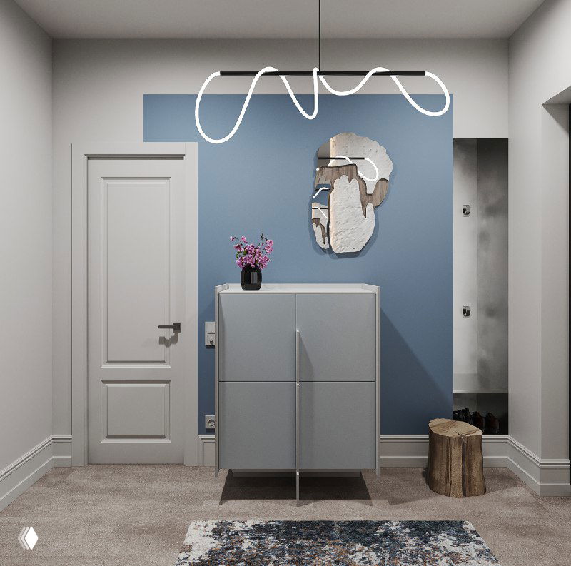 Фрагмент прихожей: светлый комод у синей акцентной стены с оригинальным зеркалом и подвесным светильником, ковер на полу и дверь слева.
