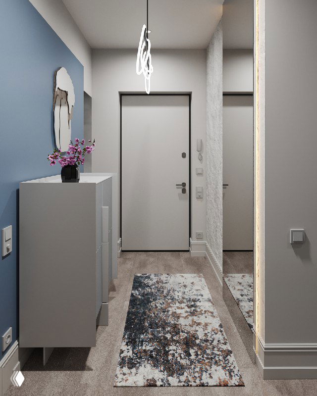 Продольный вид коридора: серая мебель у стены, ковер, входная дверь и отражение в зеркале, подчёркнутые мягким светом люстры.
