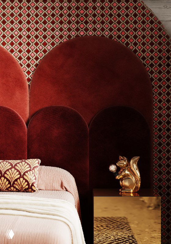 Крупный план красного бархатного изголовья в виде арок, рядом золотая тумба с декоративной фигуркой и орнамент стены — деталь спальни.