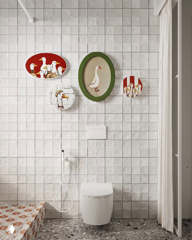 Унитаз и душевая зона на фоне глянцевой белой плитки, над ними декоративные тарелки и овальное зелёное панно с изображением птицы и гусей.