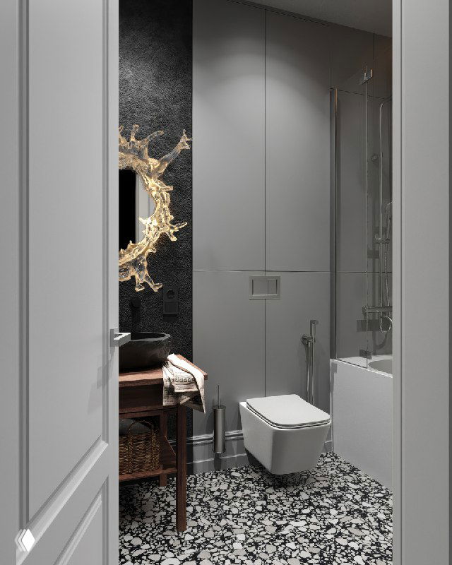 Вид компактной ванной: золотистое зеркало‑бра в форме застывших брызг, состаренная деревянная тумба и каменная раковина.