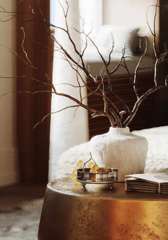 Деталь интерьера: металлический столик с вазой и сухими ветками на фоне текстиля и дерева — акцент на натуральных материалах и фактурах.