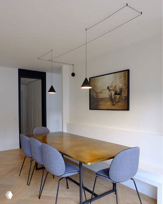 Обеденная зона с деревянным столом и подвесными лампами; потолок украшен графичной открытой проводкой как декоративный элемент интерьера.