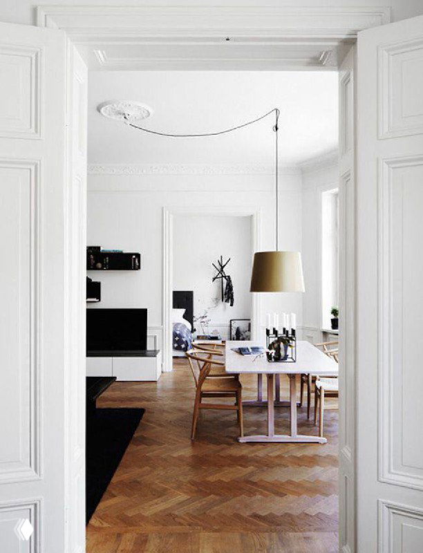 Светлая столовая с одиночной подвесной лампой и декоративной проводкой на потолке, белые двери и паркет создают спокойный скандинавский фон.