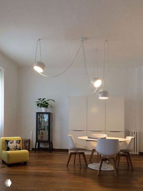 Белая гостиная с несколькими подвесными светильниками на длинных проводах; минималистичный интерьер и акцент на линии проводки.