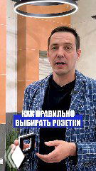 Иван Безруков показывает образец розетки на фоне интерьерной стены; фото иллюстрирует выбор цвета розеток и выключателей.